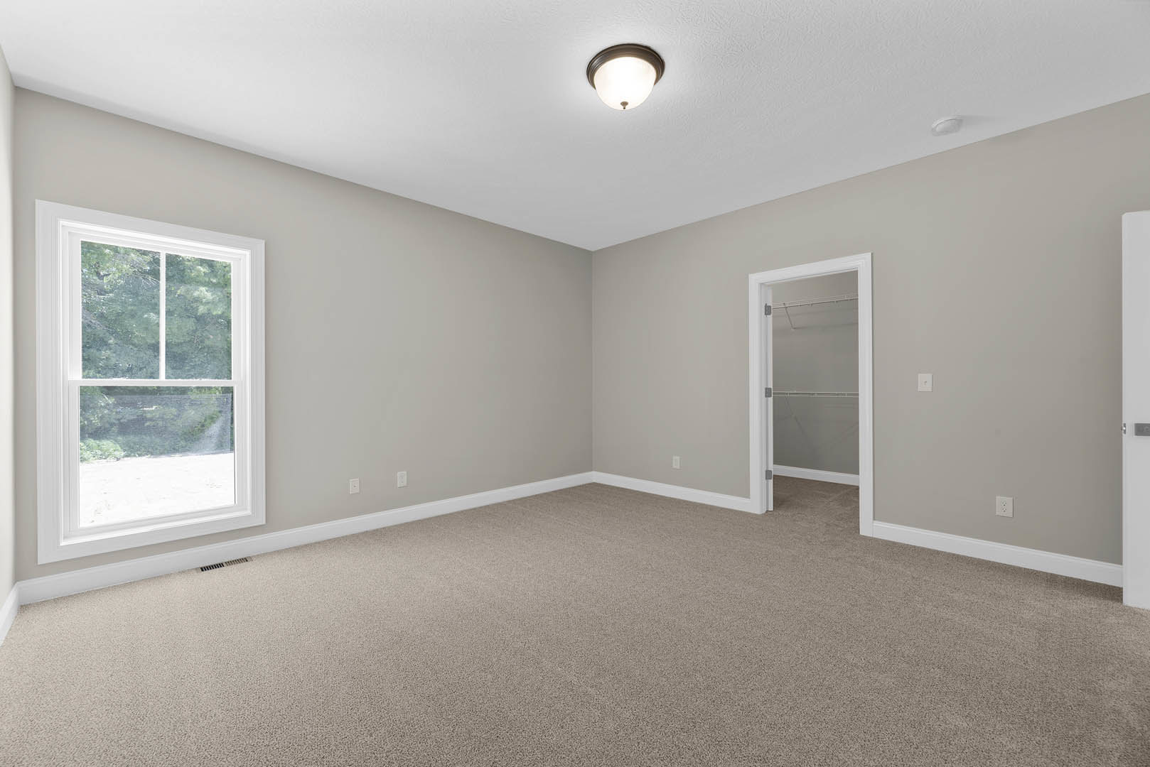 Carpeted bedroom with white walls, white door and closet, window with white frame overlooking trees, ceiling-mounted light fixture