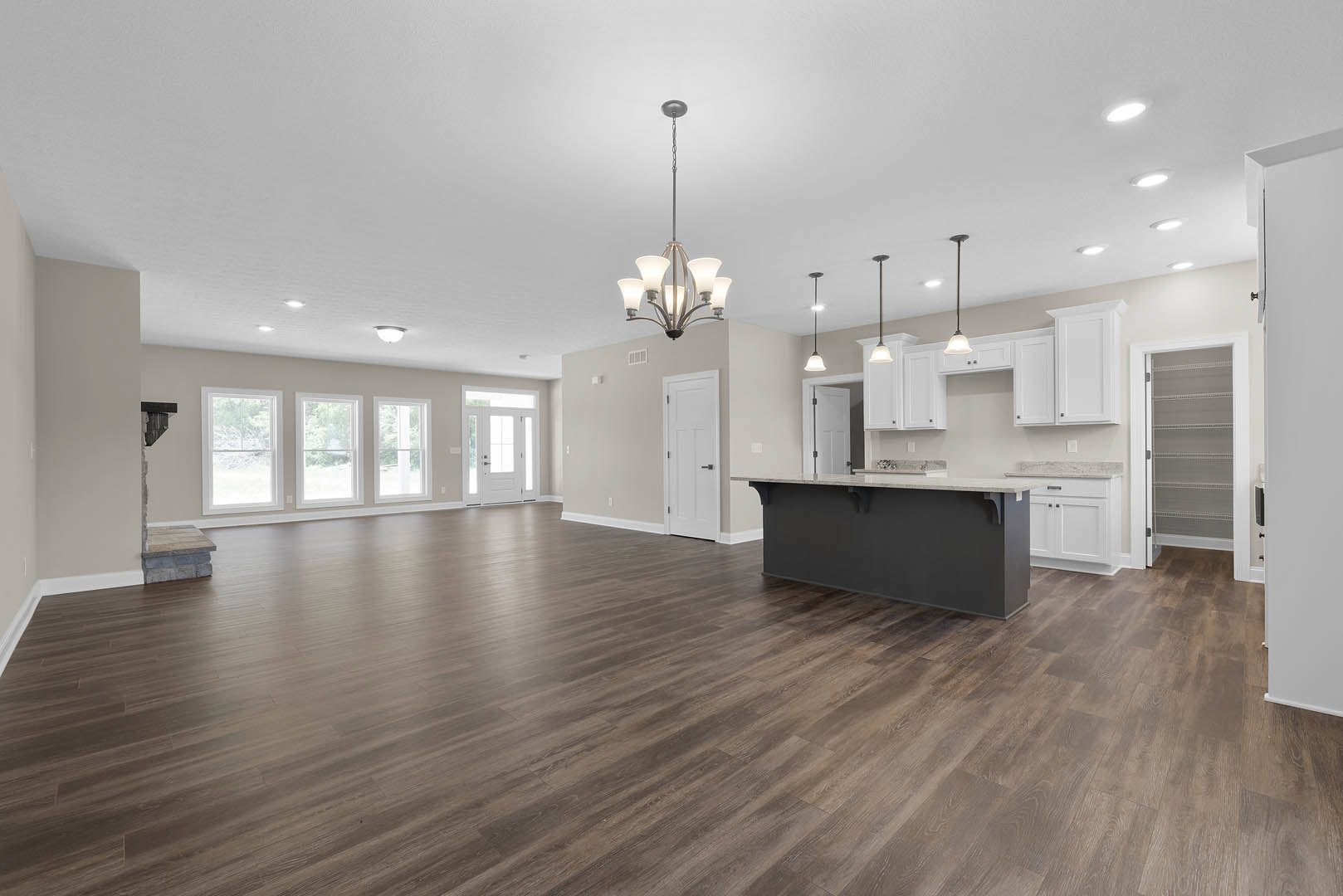 Spacious open concept kitchen and living area featuring a central kitchen island, hardwood flooring, white cabinetry, recessed lighting, and a modern chandelier.