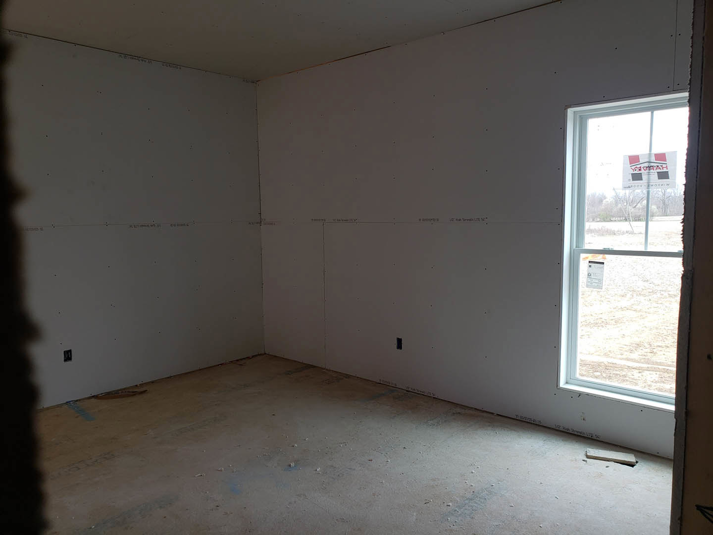 Concrete floor and white plaster walls in a minimalist room with a large window displaying a white sign.