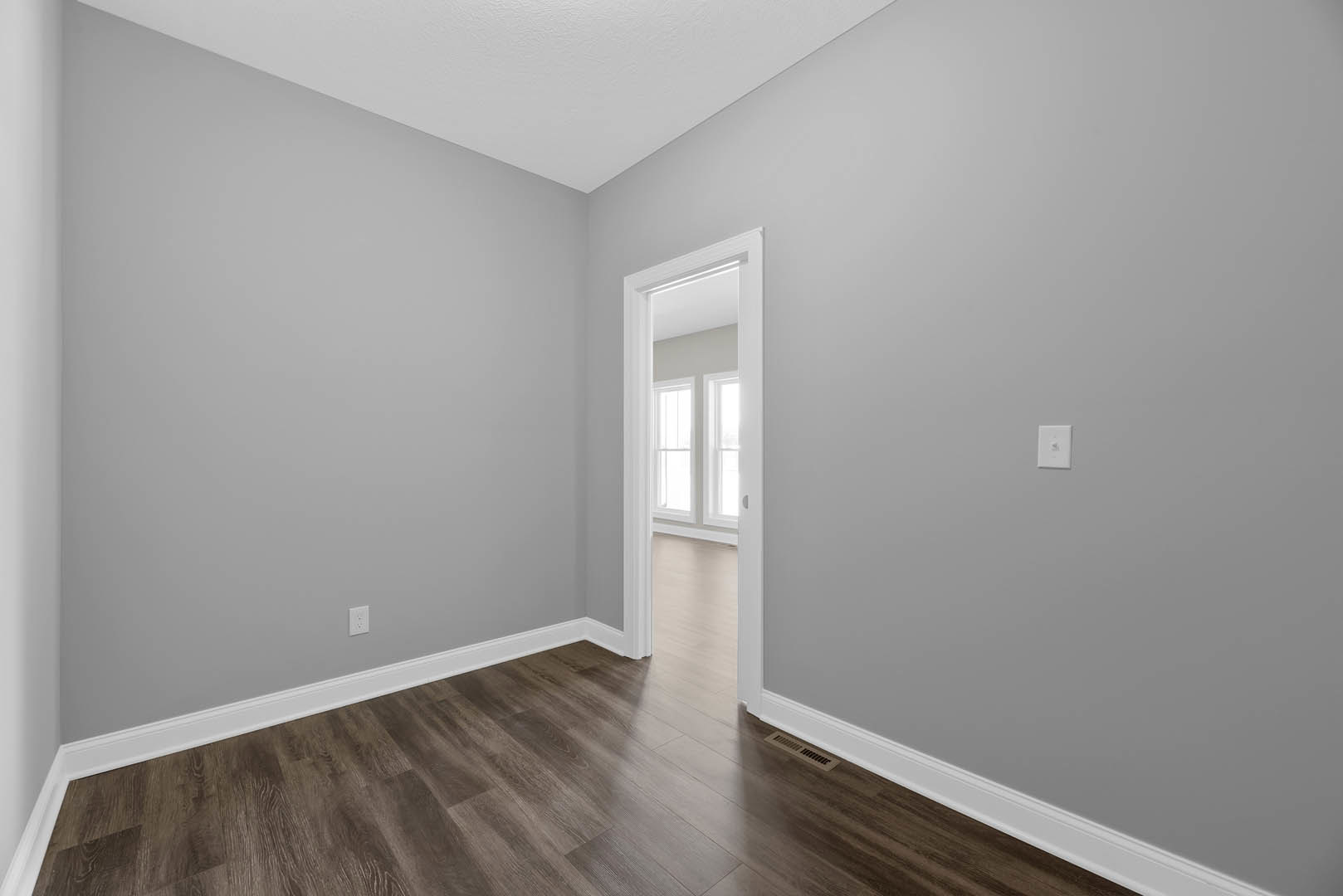 Open white door with window, wood laminate flooring and white trim, white curtain beside window, white wall switch with logo on plaster wall