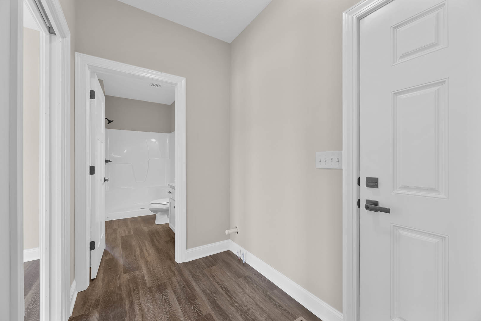 Hallway with white paneled doors, wood flooring with white baseboards, and a glimpse of a bathroom featuring a white toilet and shower