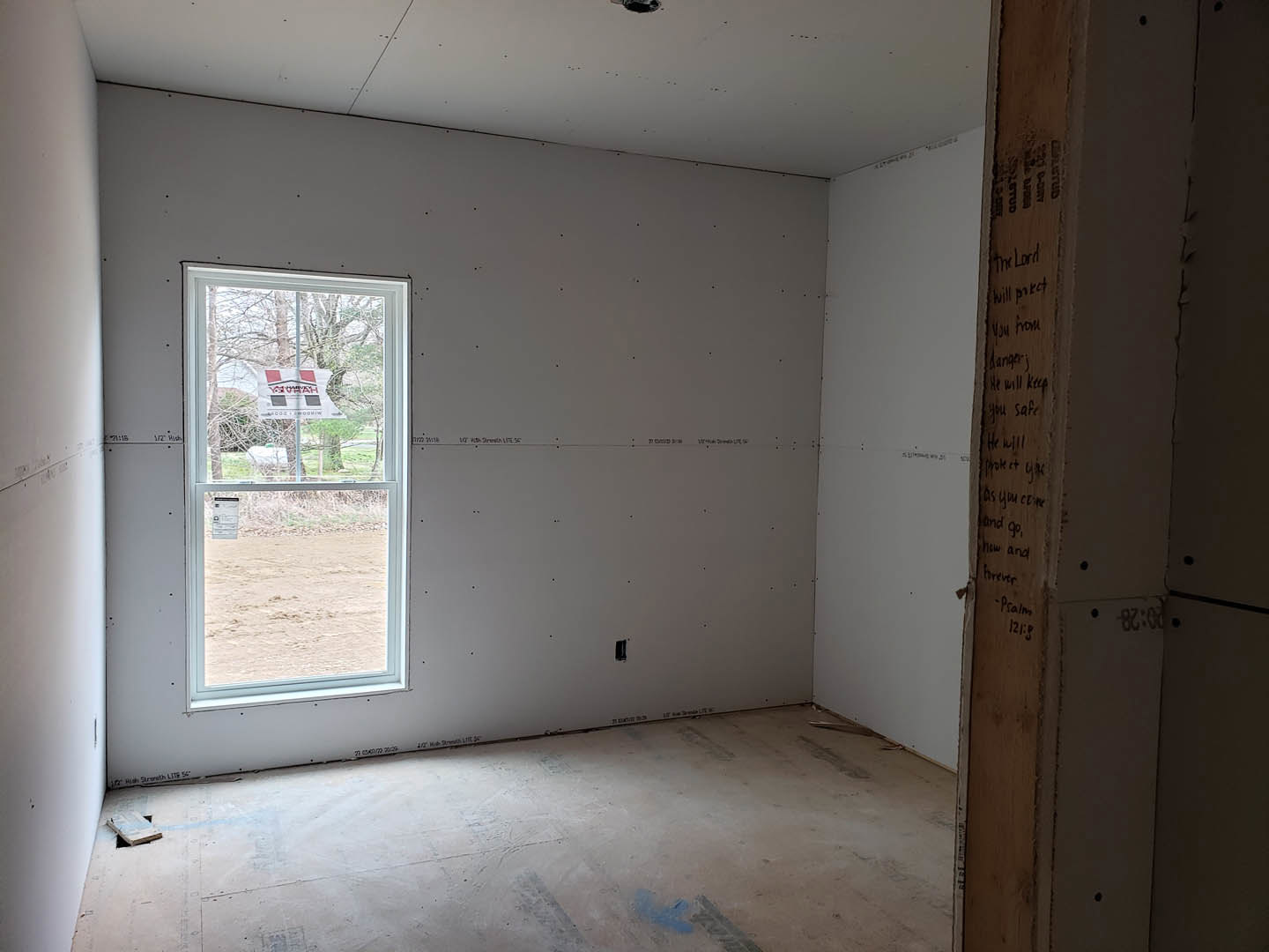 Concrete floor and plaster walls in a room with a large window displaying a sign with red and black squares.