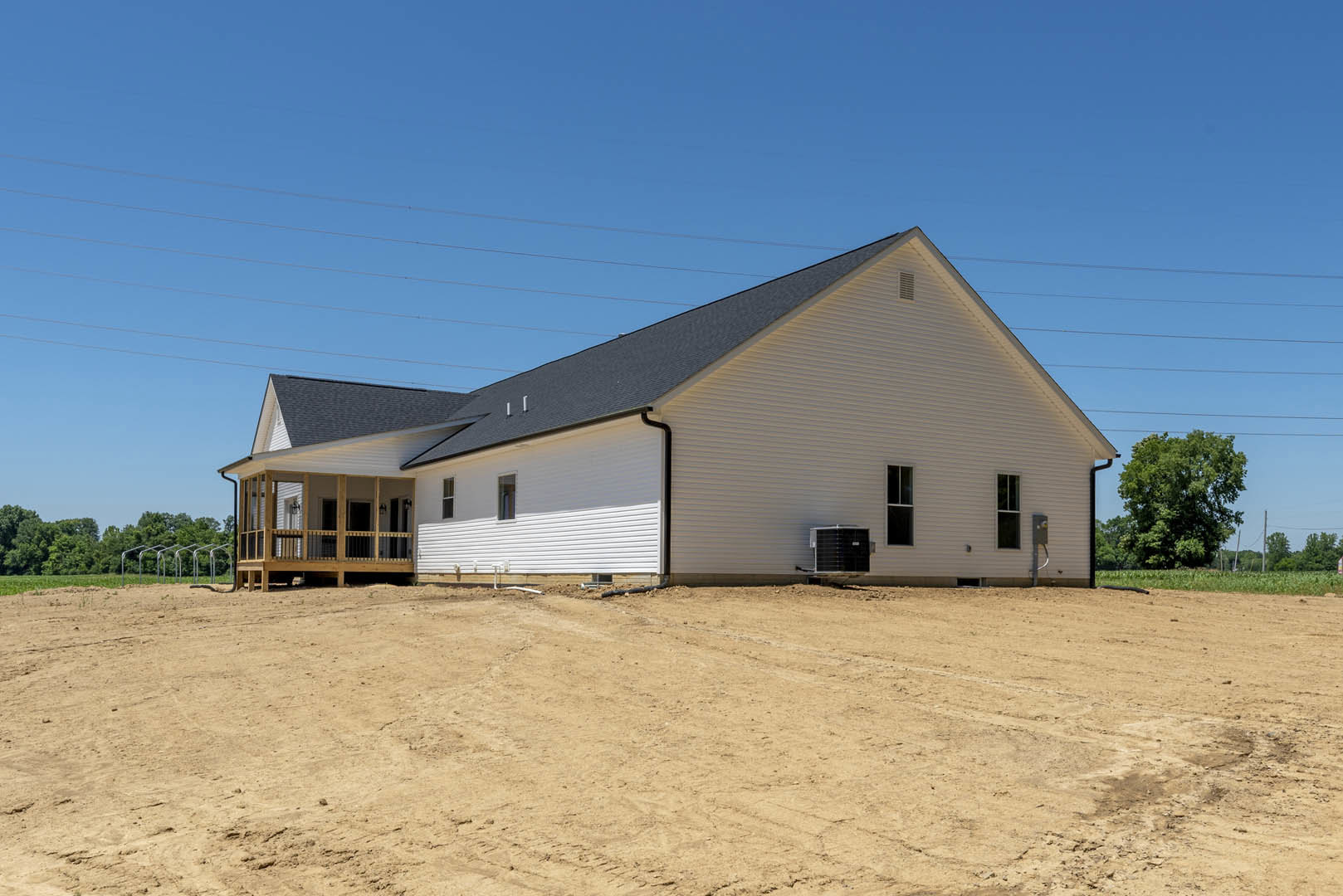 White house with black roof under construction, surrounded by dirt field, leafy tree nearby, power lines visible in background
