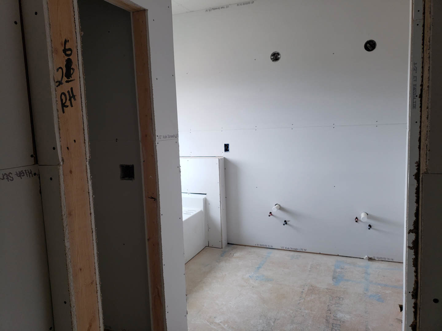 Bathroom with white plaster walls, freestanding tub, vented white rectangular fixture, and door; close-up of light-colored flooring and black square accent on wall.