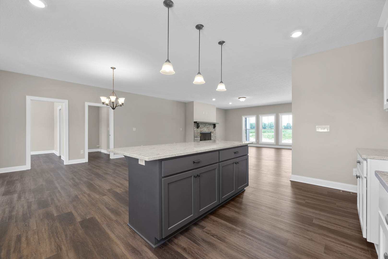 Open kitchen and living room with hardwood flooring, marble-topped kitchen island, white cabinetry, row of windows, white walls, and door frame