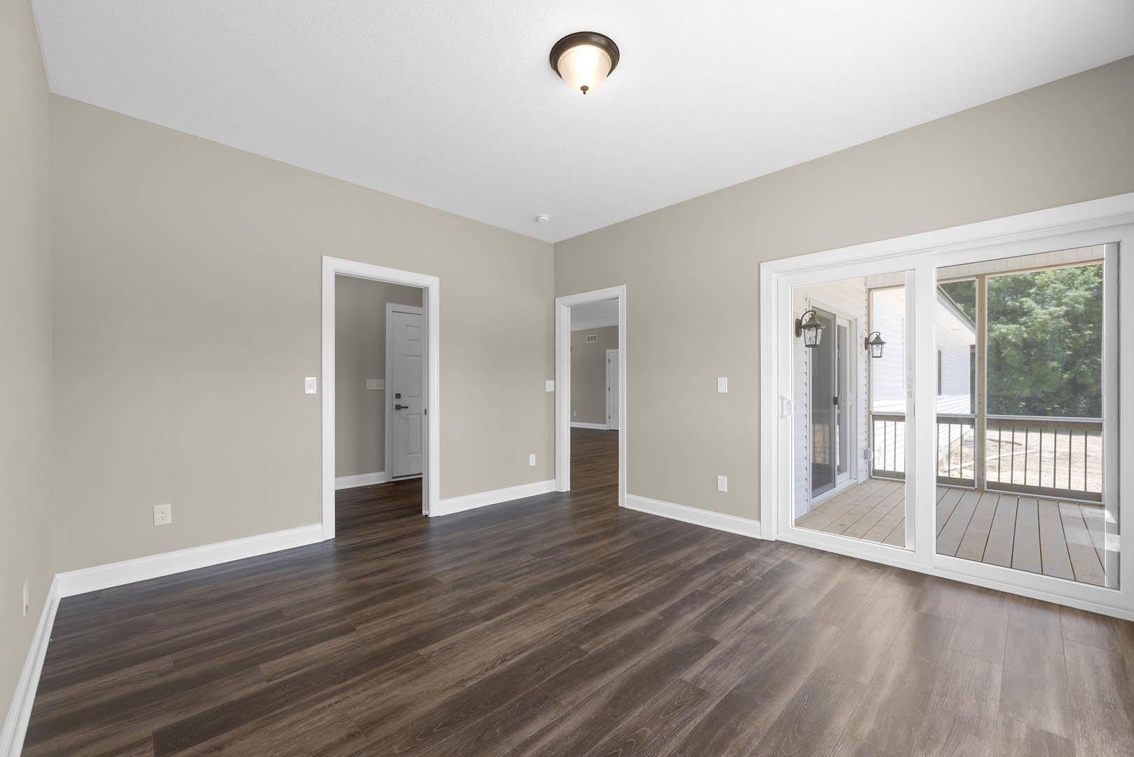 Wood floor with white trim, sliding glass door opening to deck, white door with black handles, ceiling light fixture, window overlooking trees