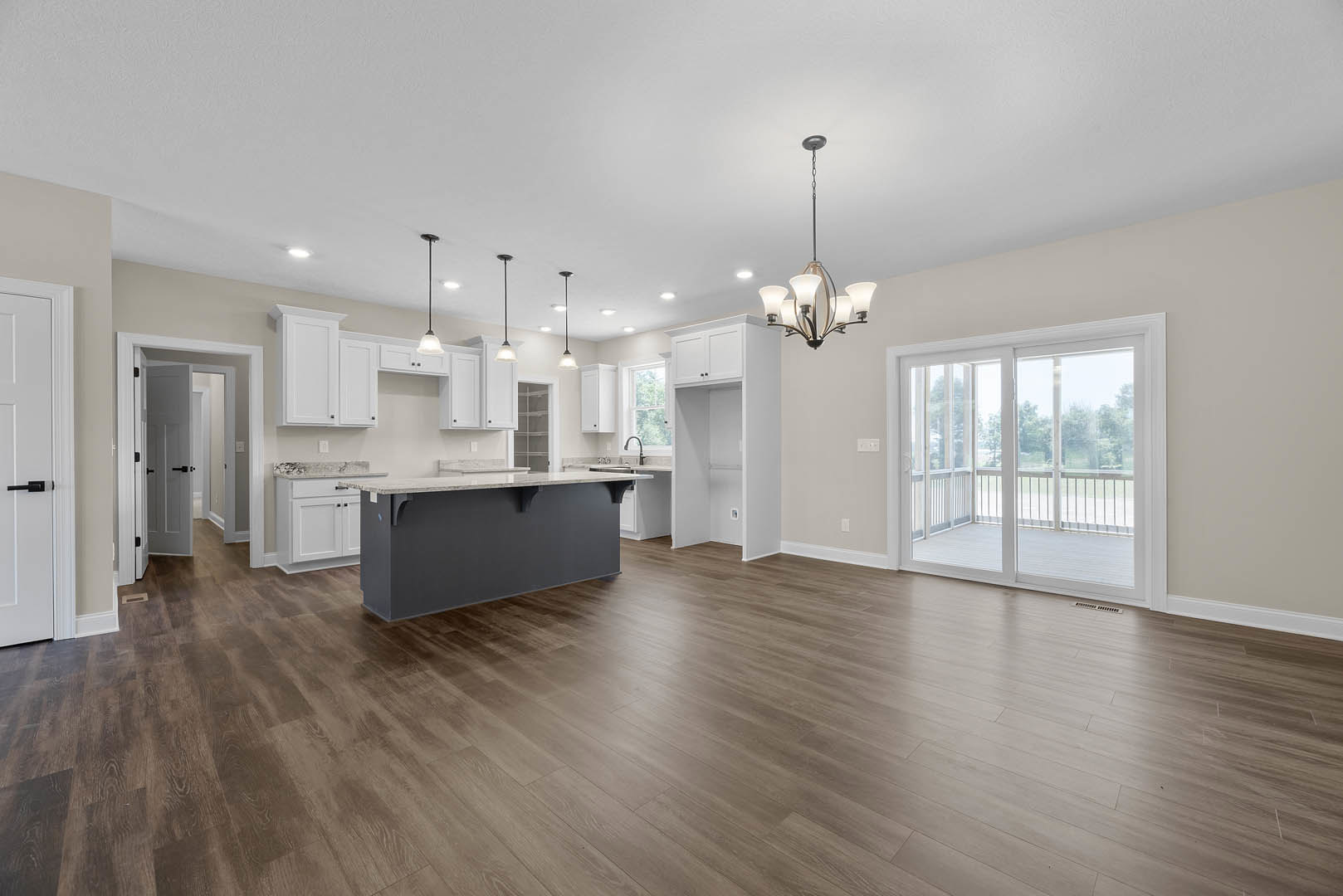 Spacious open-concept kitchen with marble-topped island, hardwood flooring, white cabinetry, sliding glass door, and modern chandelier