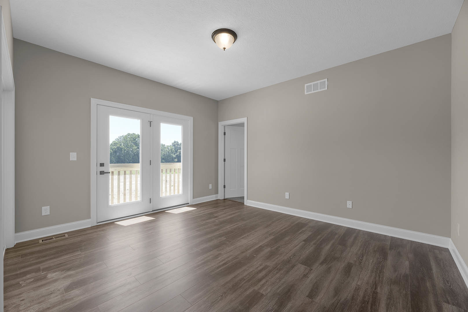 Wood flooring in a bright room with a white double door featuring glass panes, metal handles, and a white-framed window; ceiling light fixture overhead.