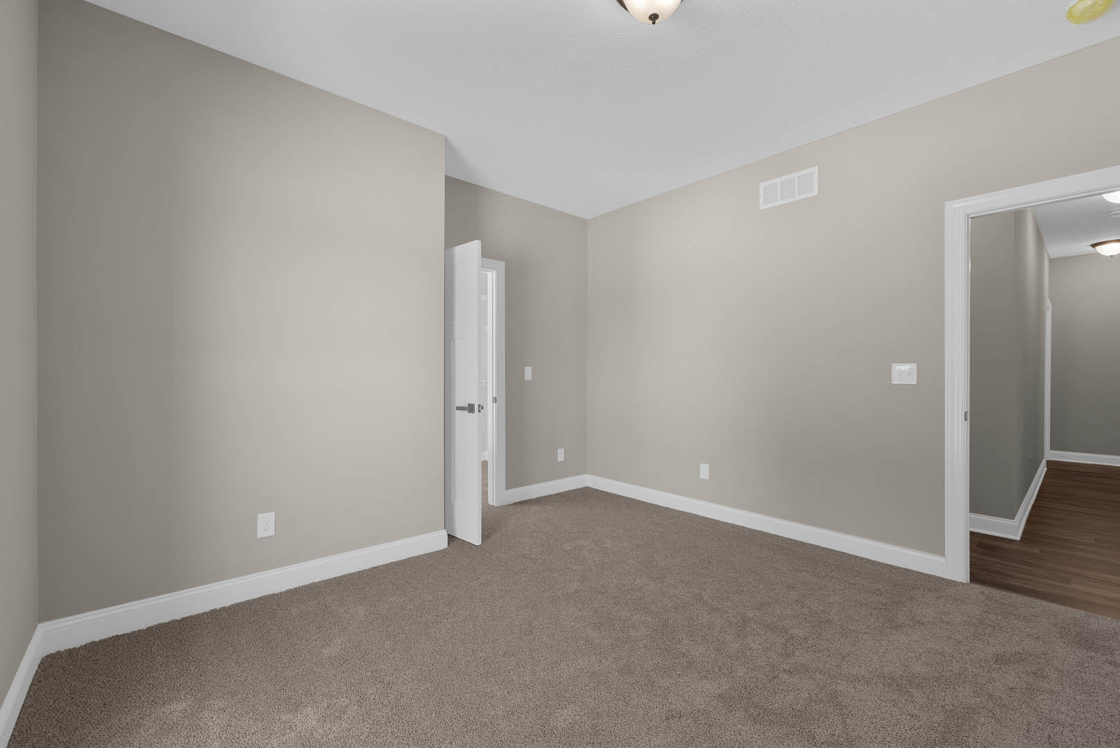 Carpeted room with white walls, open white door featuring a silver handle, wood laminate flooring, and a window with glass panels