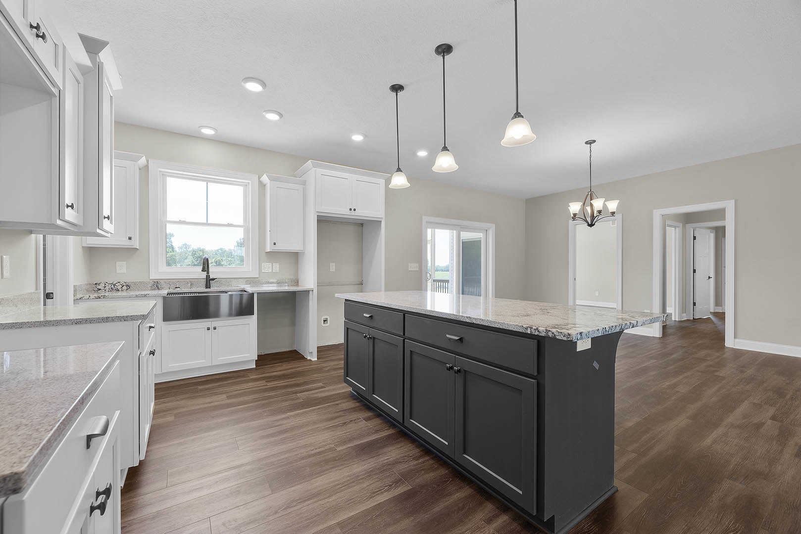 Spacious kitchen featuring a large marble-topped island, white cabinetry, stainless steel appliances, tile backsplash, and a sink positioned beneath a window.