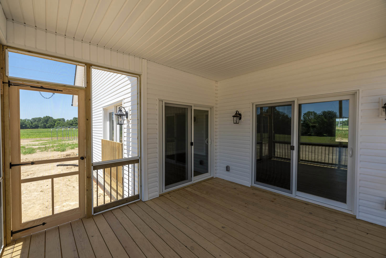 White siding house with wooden deck, sliding glass door, screen door with chain, and exterior lamp fixture