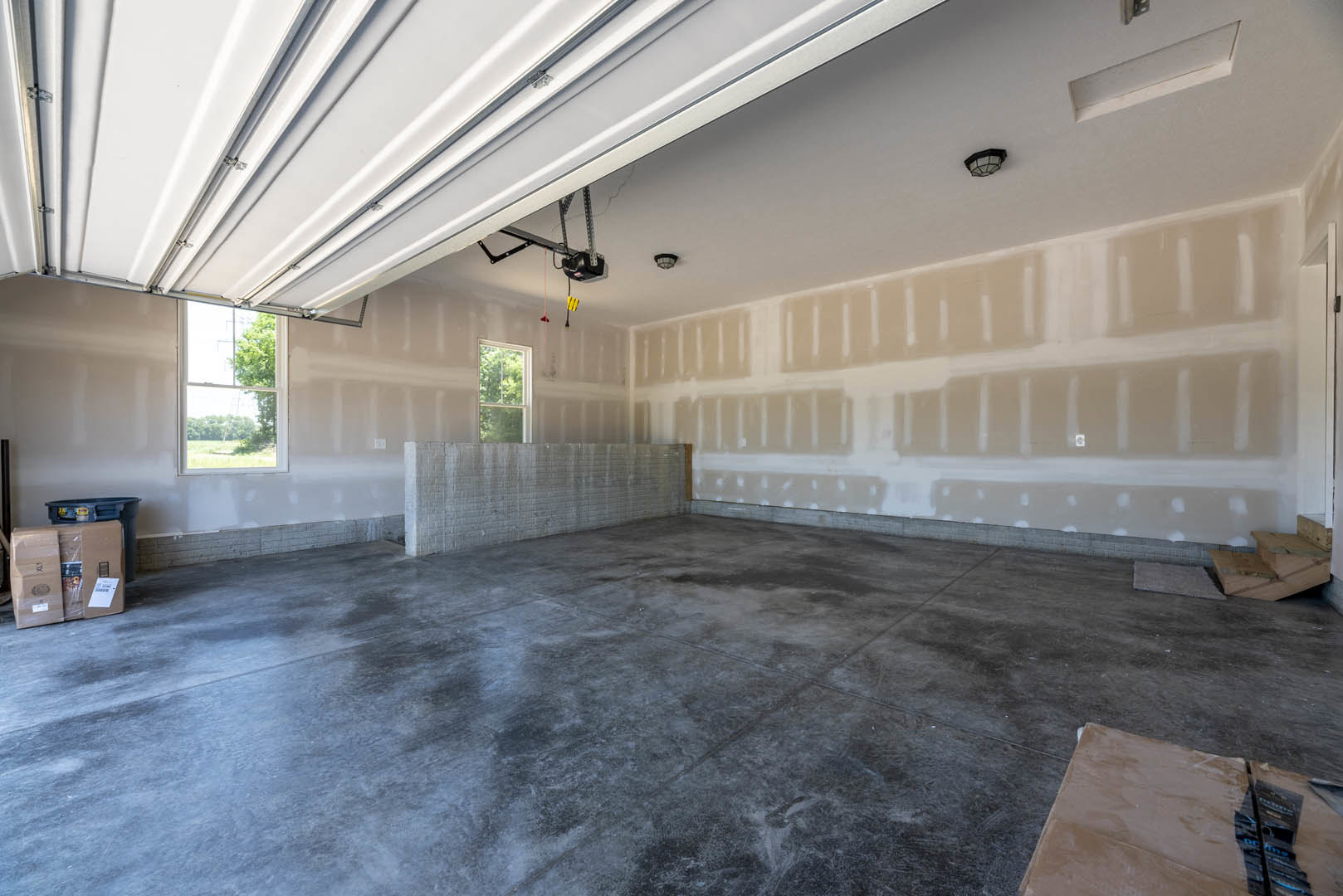 Concrete floor room with white plaster walls, ceiling beams, garage door opener, and window overlooking trees