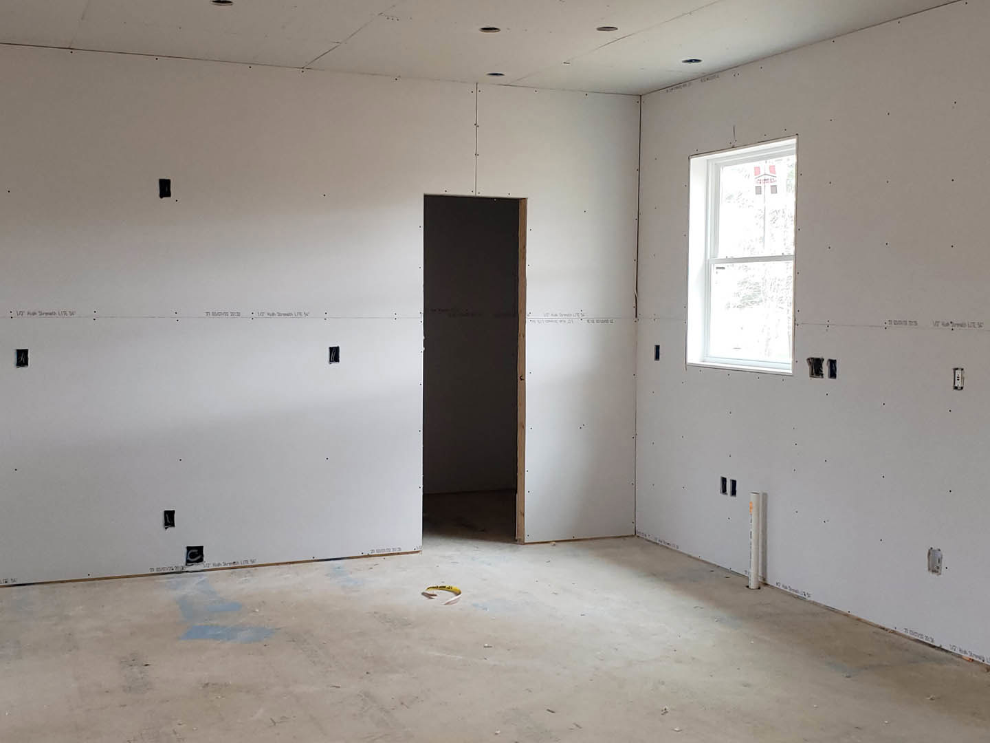 Modern interior room featuring a white-framed window, wooden-framed blackboard, yellow tape marking on concrete floor, white plaster walls, and a white ceiling with recessed holes.