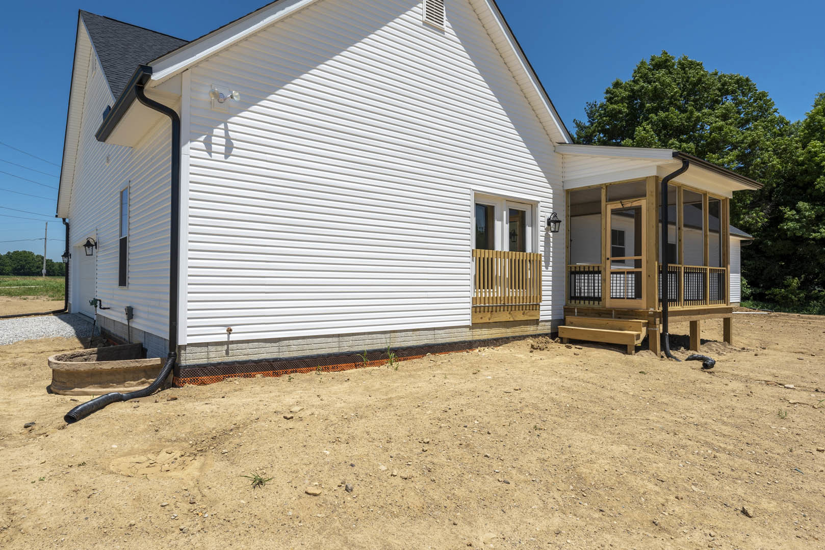 White house with horizontal siding, covered front porch supported by wooden posts, single door and window, dirt yard in foreground, small lamp post near porch, wooden fence