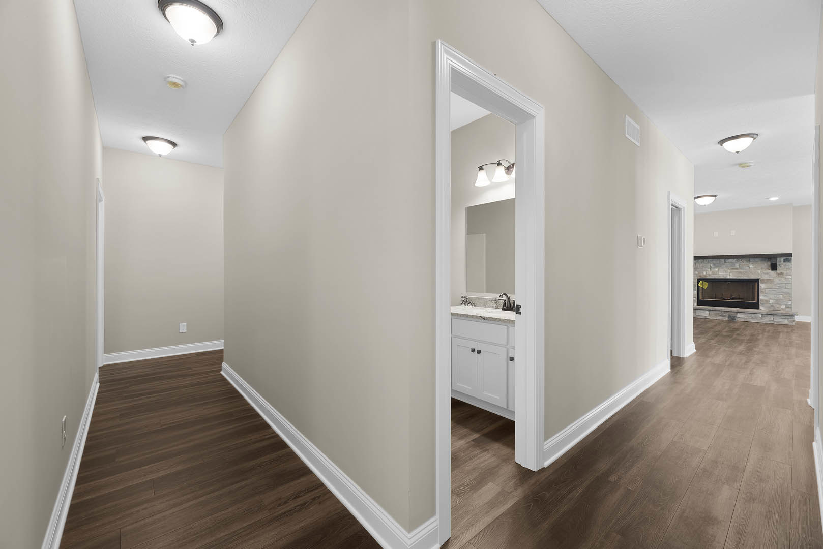 Hallway with wood flooring, plaster walls, open door, white cabinetry, and ceiling light fixture