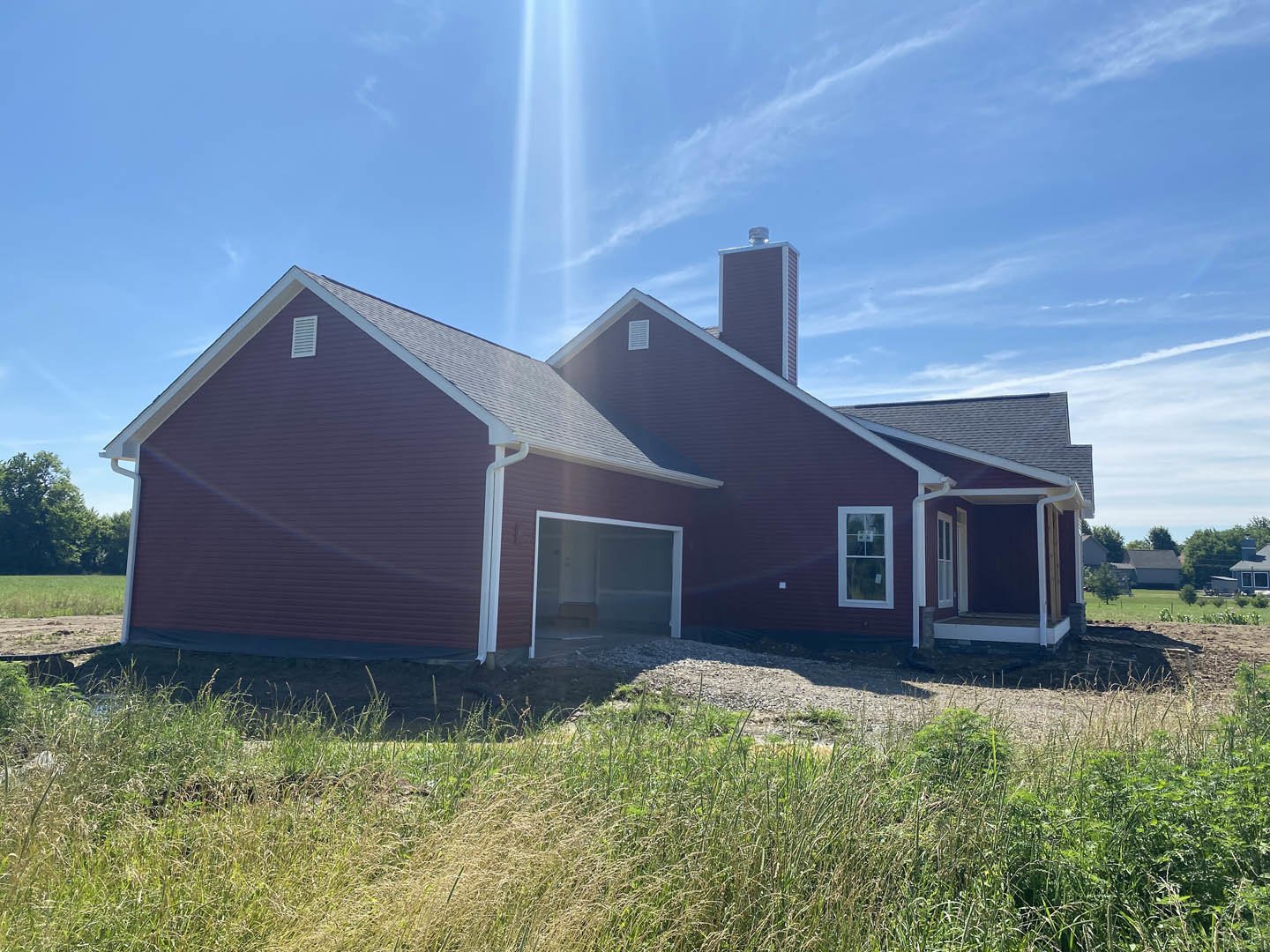 Partially built house with exposed framing, white window trim, attached garage, green grass lawn, brick chimney, and clear blue sky