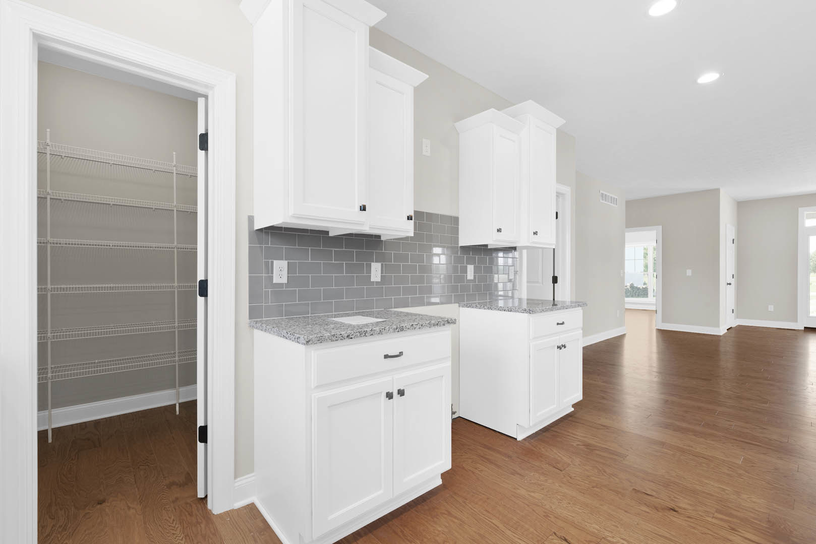 White kitchen with shaker cabinets, gray tile backsplash, marble countertop, black cabinet handles, glass-paneled door, and light wood flooring.