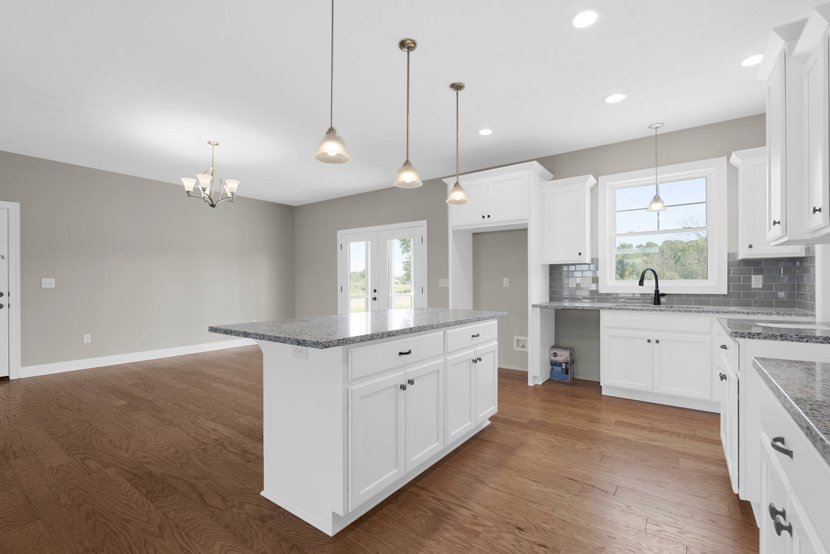 Spacious kitchen featuring a large granite island with built-in sink and faucet, white cabinetry, double glass doors, and pendant ceiling lights