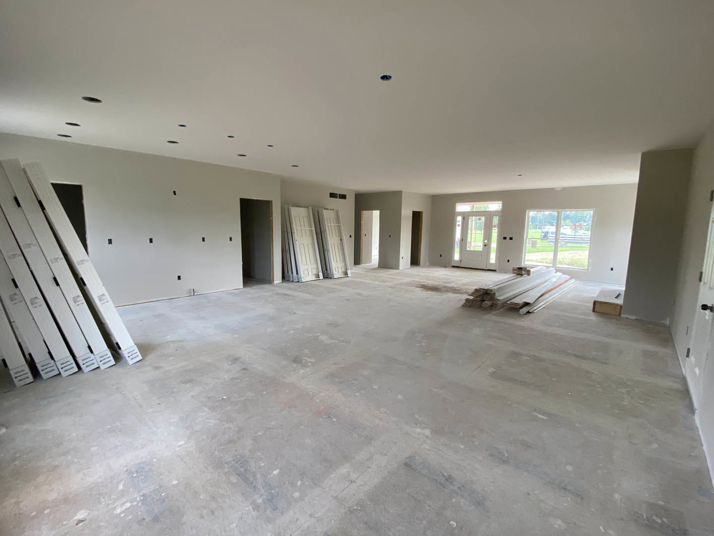 White-walled room with white ceiling, multiple white doors including one with glass panes, and stacked white boards on light flooring