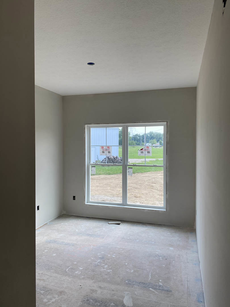 Concrete floor and white plaster walls in a room with a large window featuring signage, natural daylight illuminating minimalist interior finishes.