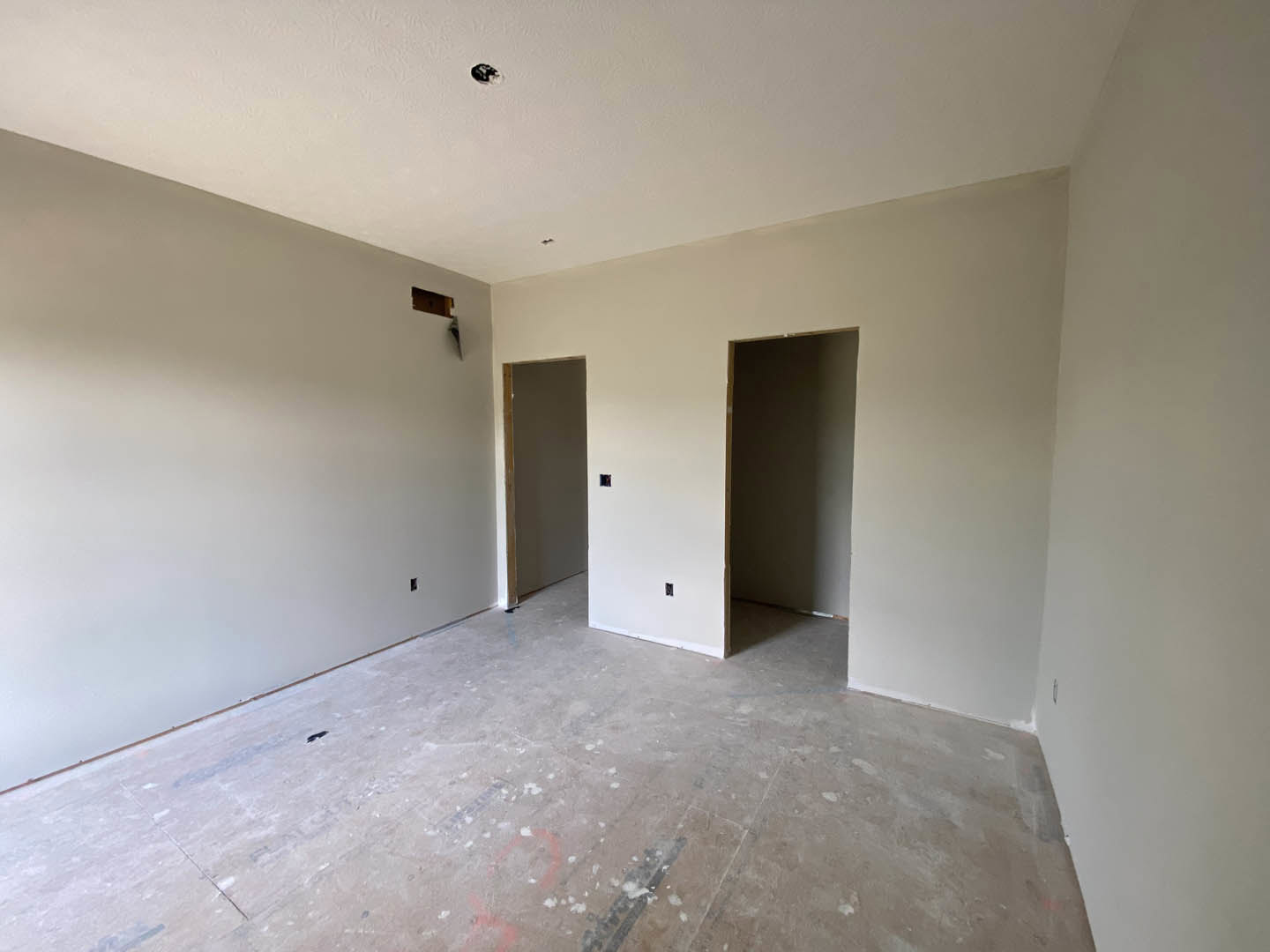 White plaster wall with wooden door frame, concrete floor, and two doors; visible paint marks on white flooring and hole in wall.