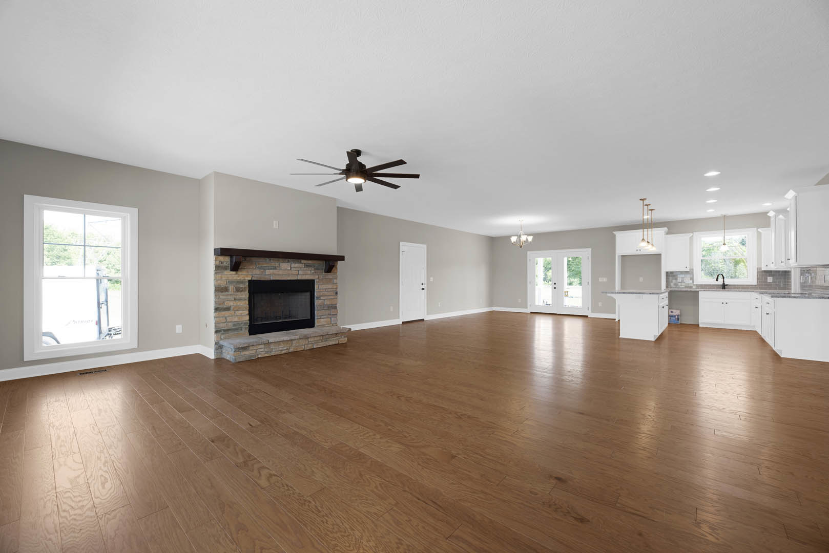 Spacious living room featuring hardwood floors, black-framed fireplace, ceiling fan with light, white-framed window, and double doors