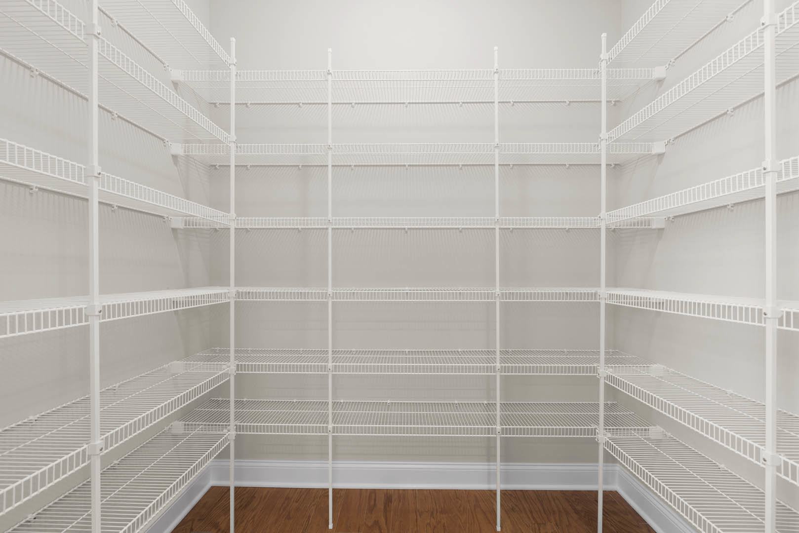 White built-in shelving unit with multiple shelves in a large empty closet, wood flooring and white baseboard visible along the wall.