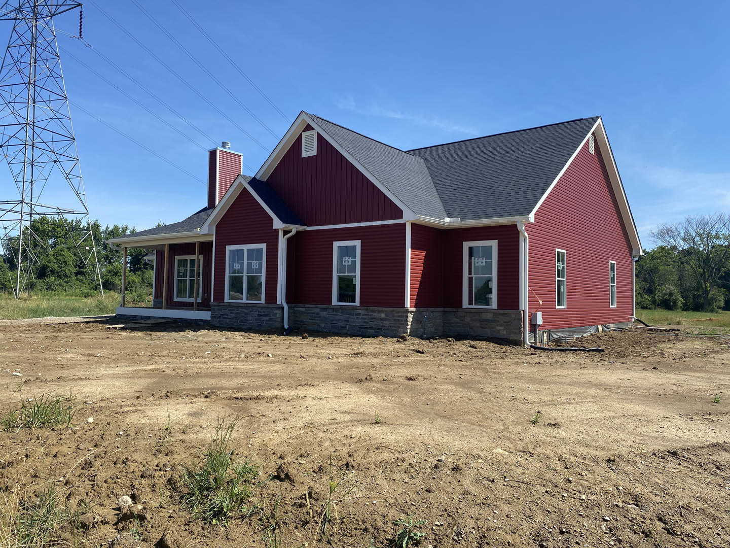 Red siding house with white-framed windows, leafless tree, dirt yard with patches of grass, and power line tower in background