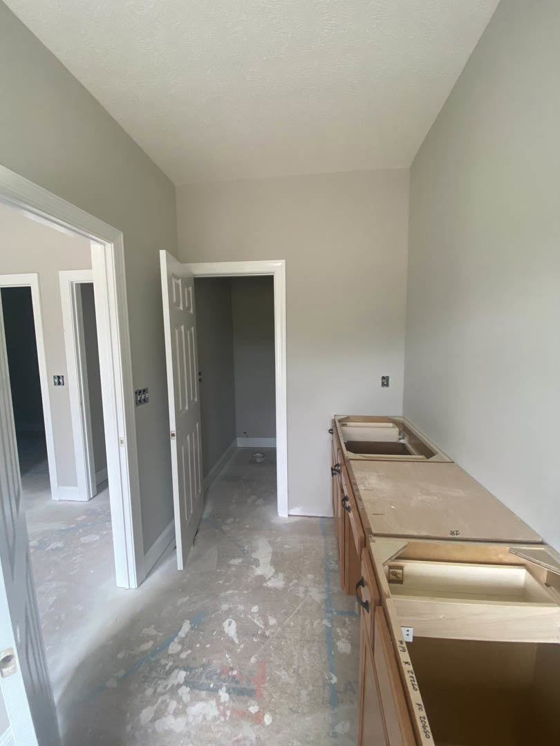 Modern kitchen featuring a stone countertop with built-in drawers, white door, and light-colored plaster walls; floor shows scattered white paint marks.