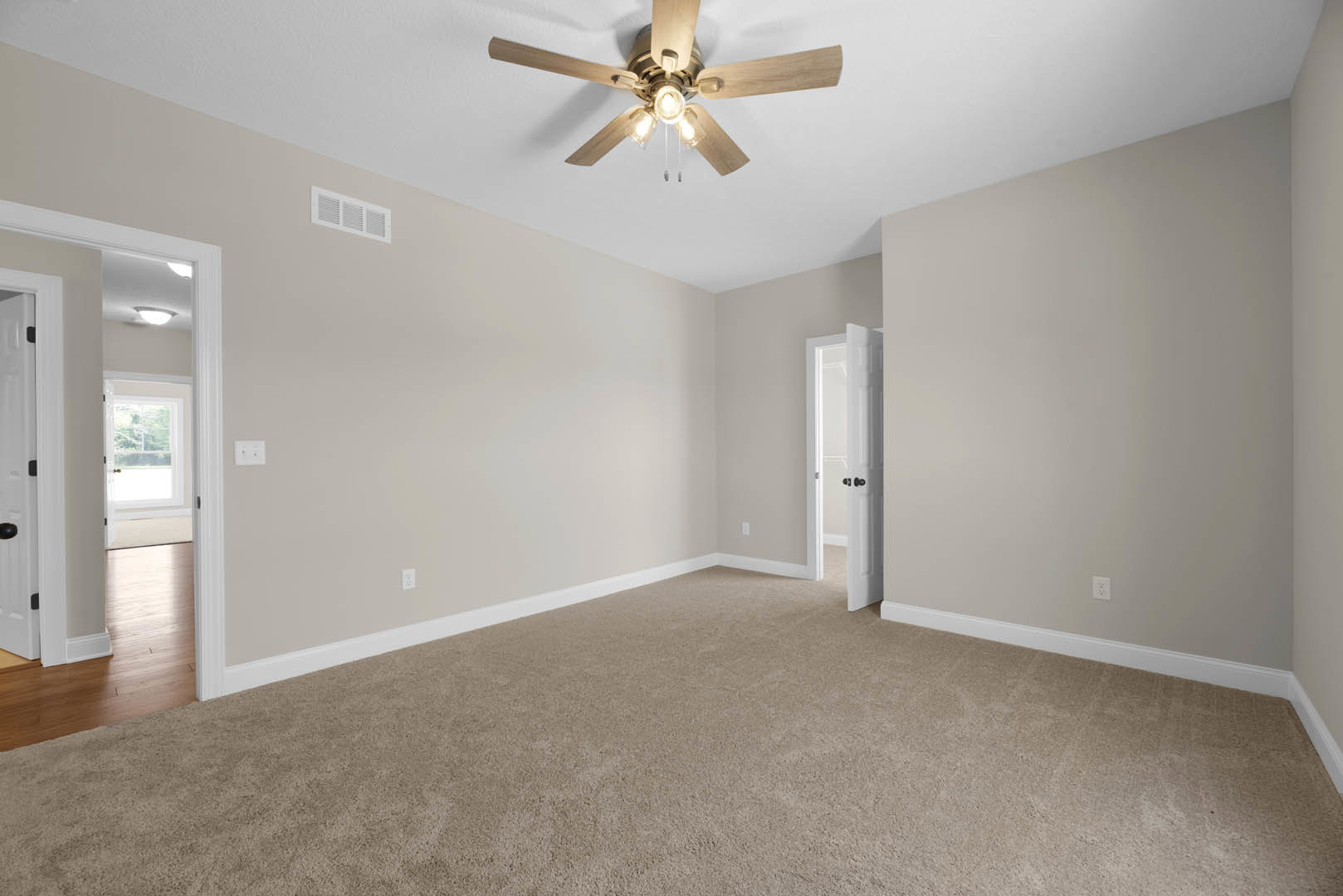 Carpeted room with white trim, ceiling fan with light bulbs, white door with black knobs and window