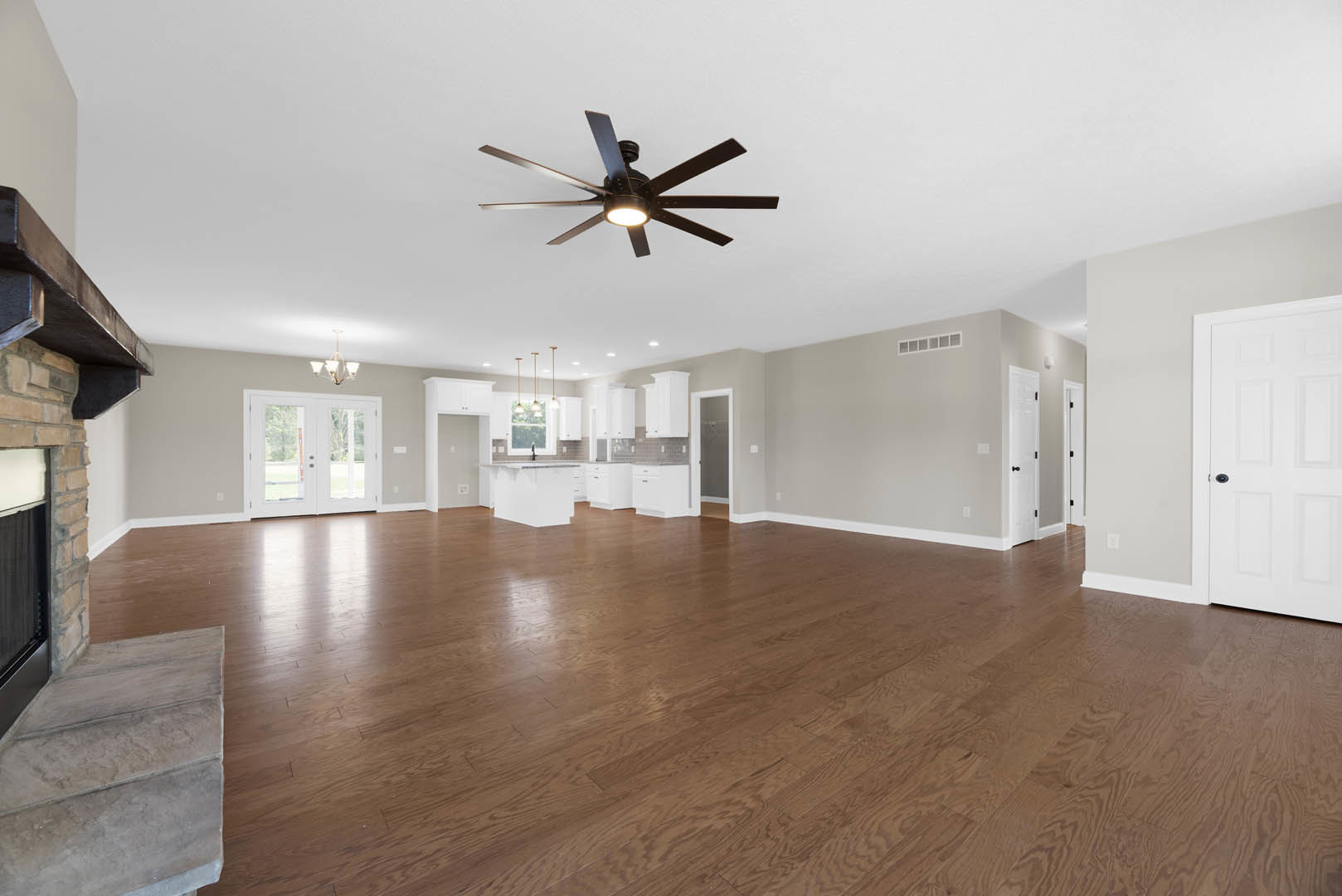Spacious room featuring hardwood flooring, ceiling fan with light fixture, double glass-paneled doors, white door with black handle, and a close-up of textured stone wall.