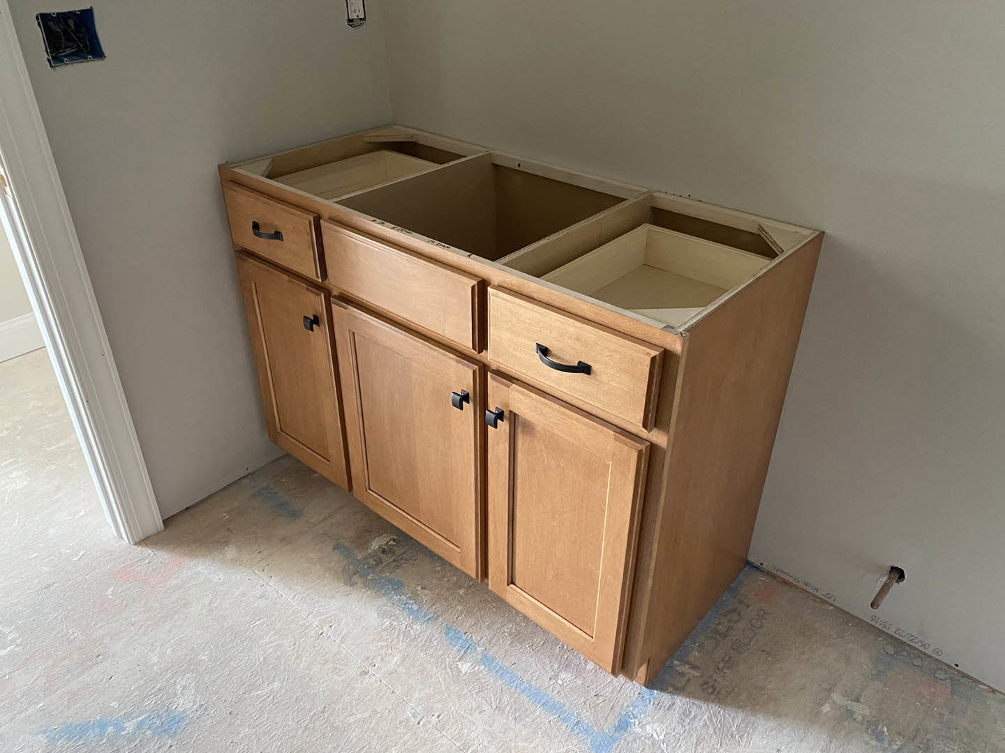 Light wood kitchen cabinet with multiple drawers, brushed metal handles, and smooth finish, set against a neutral wall and tile floor.