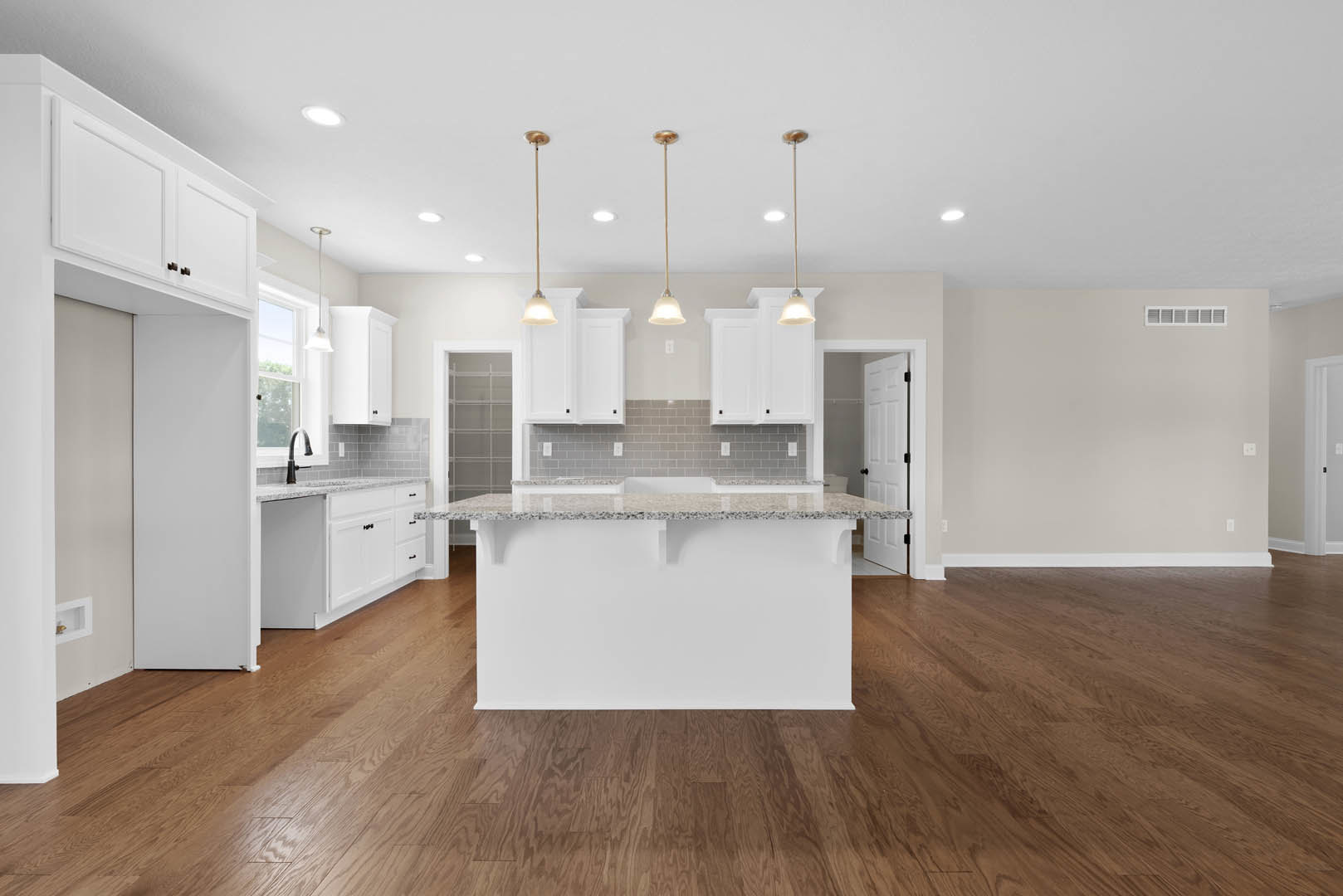 Open kitchen with white countertop bar, wood flooring, white cabinetry, black hardware, built-in shelf displaying a gold decorative object, and white walls.