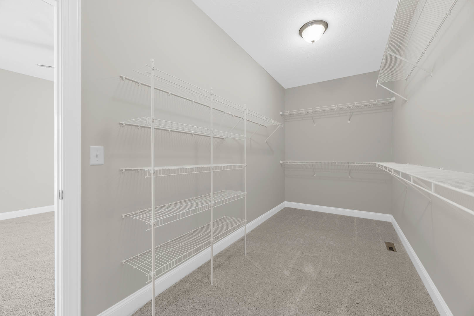 White built-in metal shelves mounted on a plaster wall, light switch nearby, ceiling with recessed light fixture, smooth flooring.