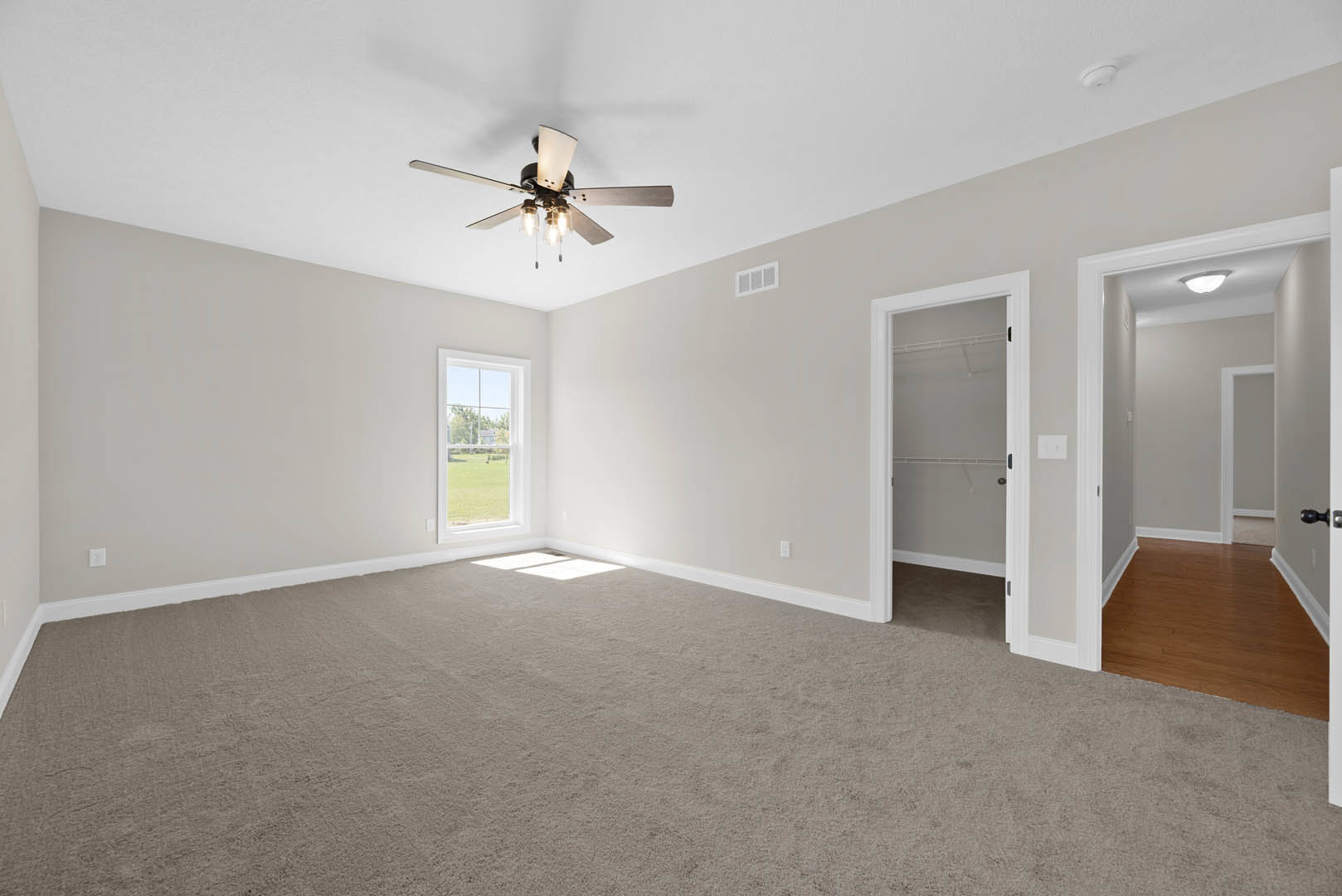 Carpeted room with white-framed door, ceiling fan with lights, wall vent, and window overlooking green lawn