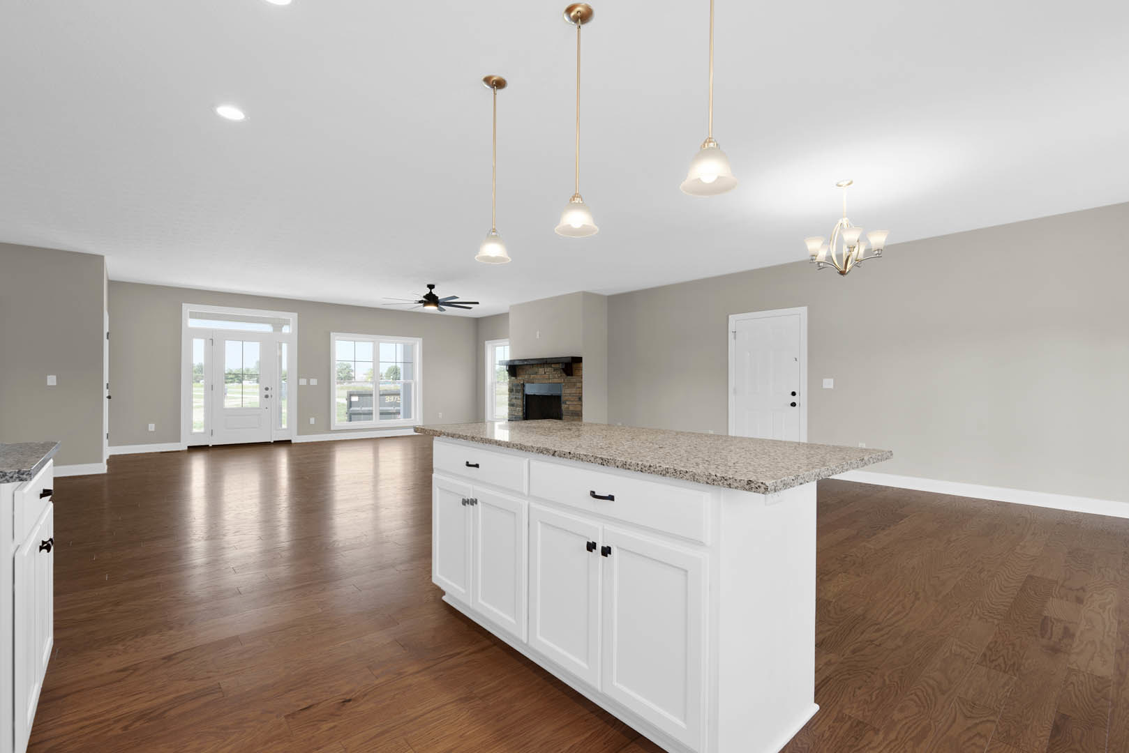 White kitchen with large central island featuring black handles, shaker cabinetry, glass-paneled door, light wood flooring, and window overlooking outdoor container.