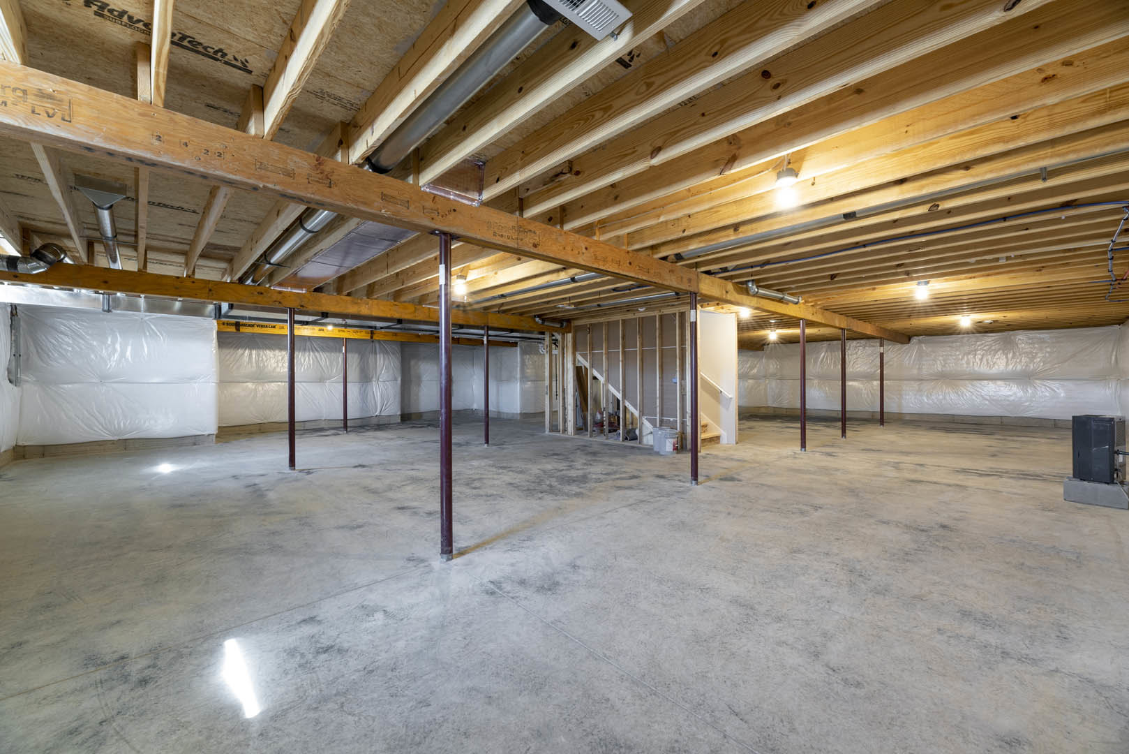 Exposed wooden beams and wood ceiling above unfinished concrete floor with red support poles in an empty basement room