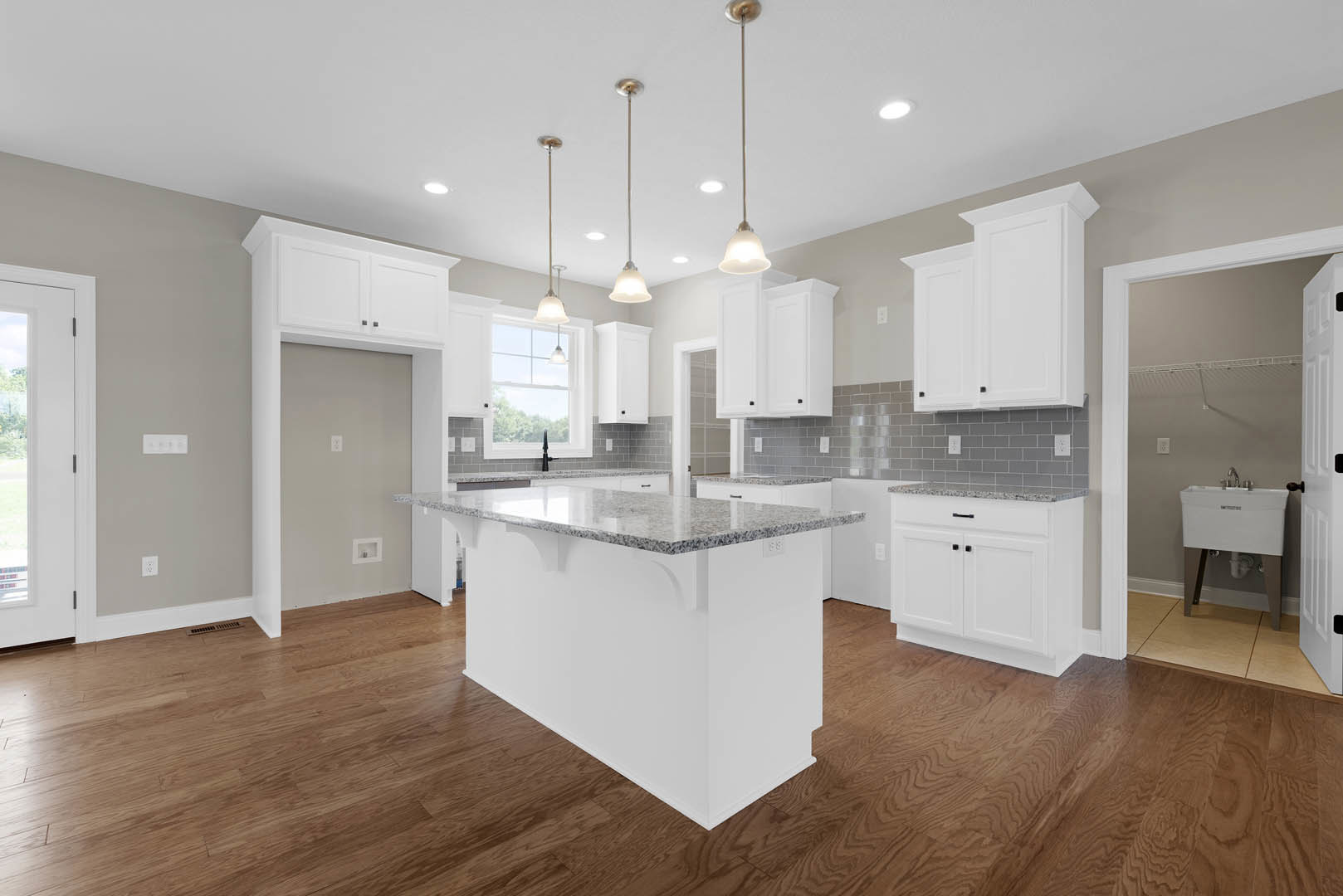White kitchen with hardwood flooring, central island featuring granite countertop, undermount sink beneath wall, white cabinetry with marble tops, white door with window, pole with