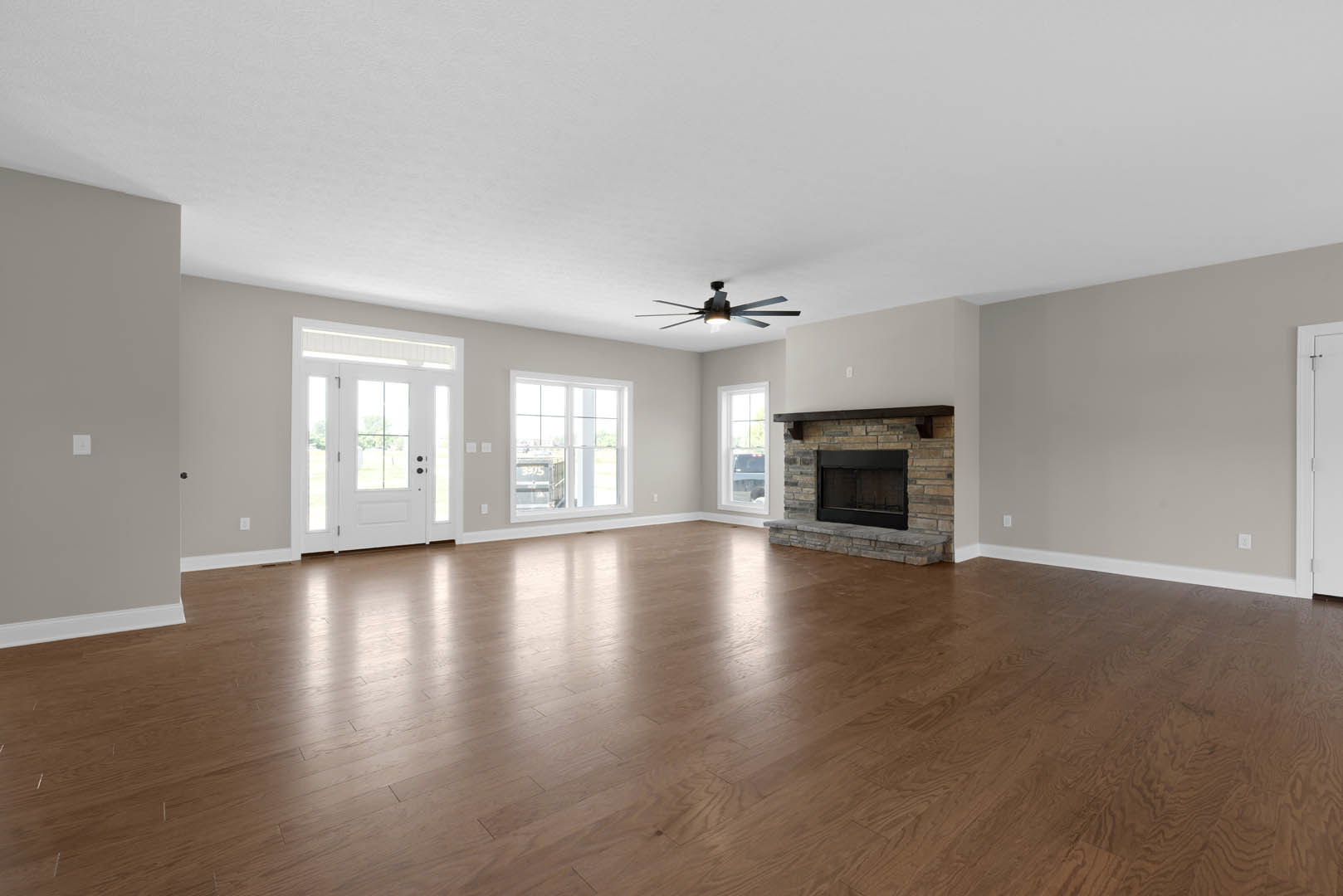 Living room with hardwood floors, stone fireplace, ceiling fan with light, white door with glass panes, and window