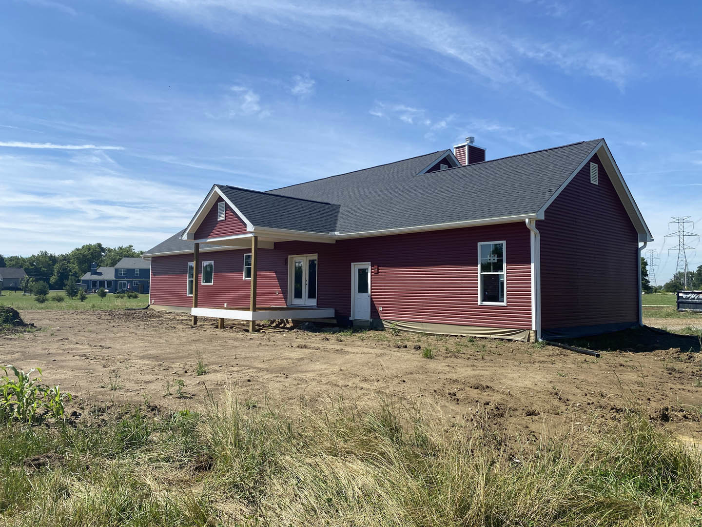 Red house with white trim and glass-paneled door, basketball hoop mounted in window, dirt field in foreground, blue sky with scattered clouds above