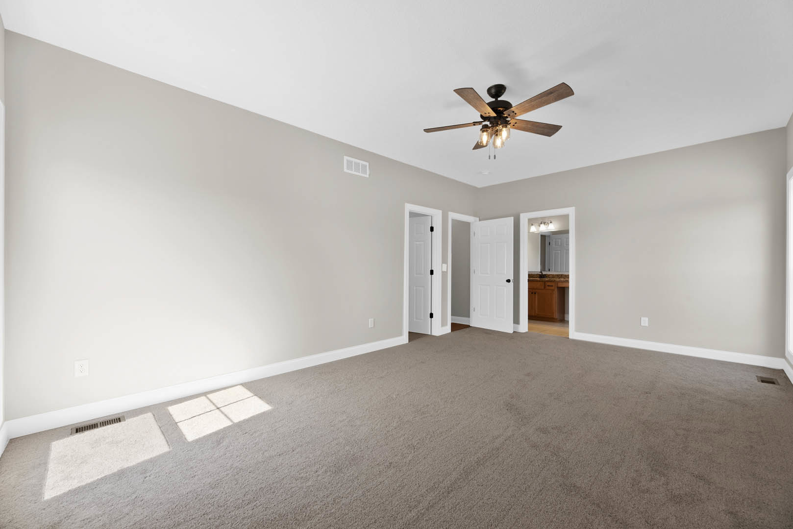 Carpeted room with white walls, ceiling fan with light fixture, white door featuring black handle and knobs