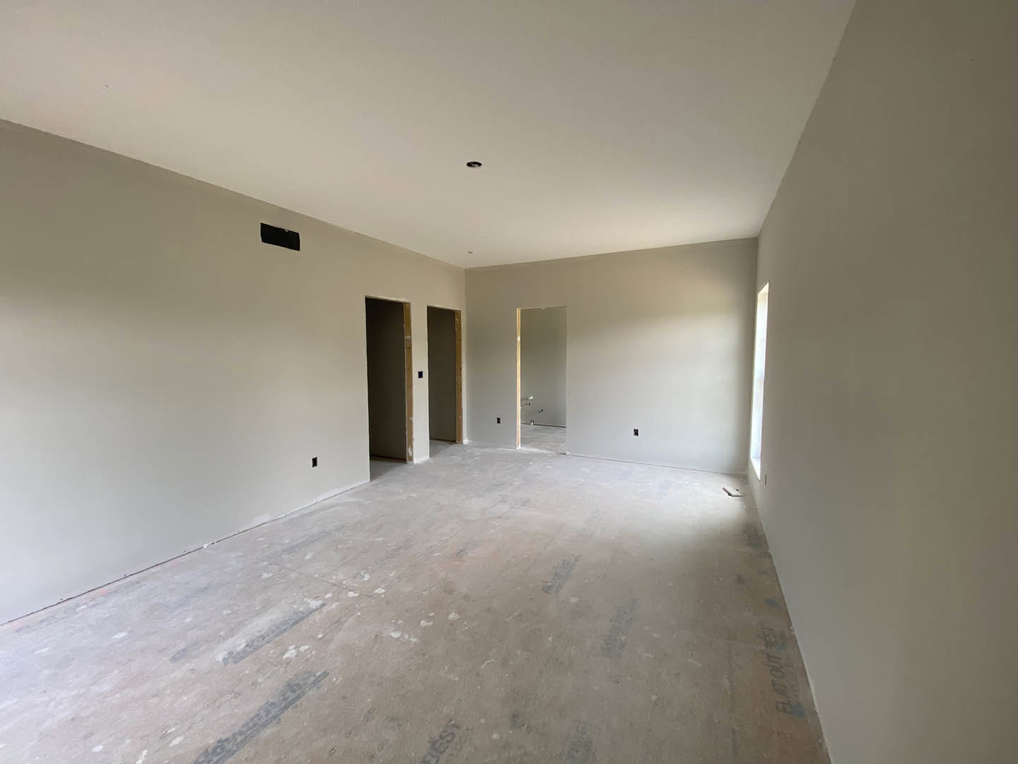 White-walled room with open white door featuring black frame, white flooring, and large window letting in natural light