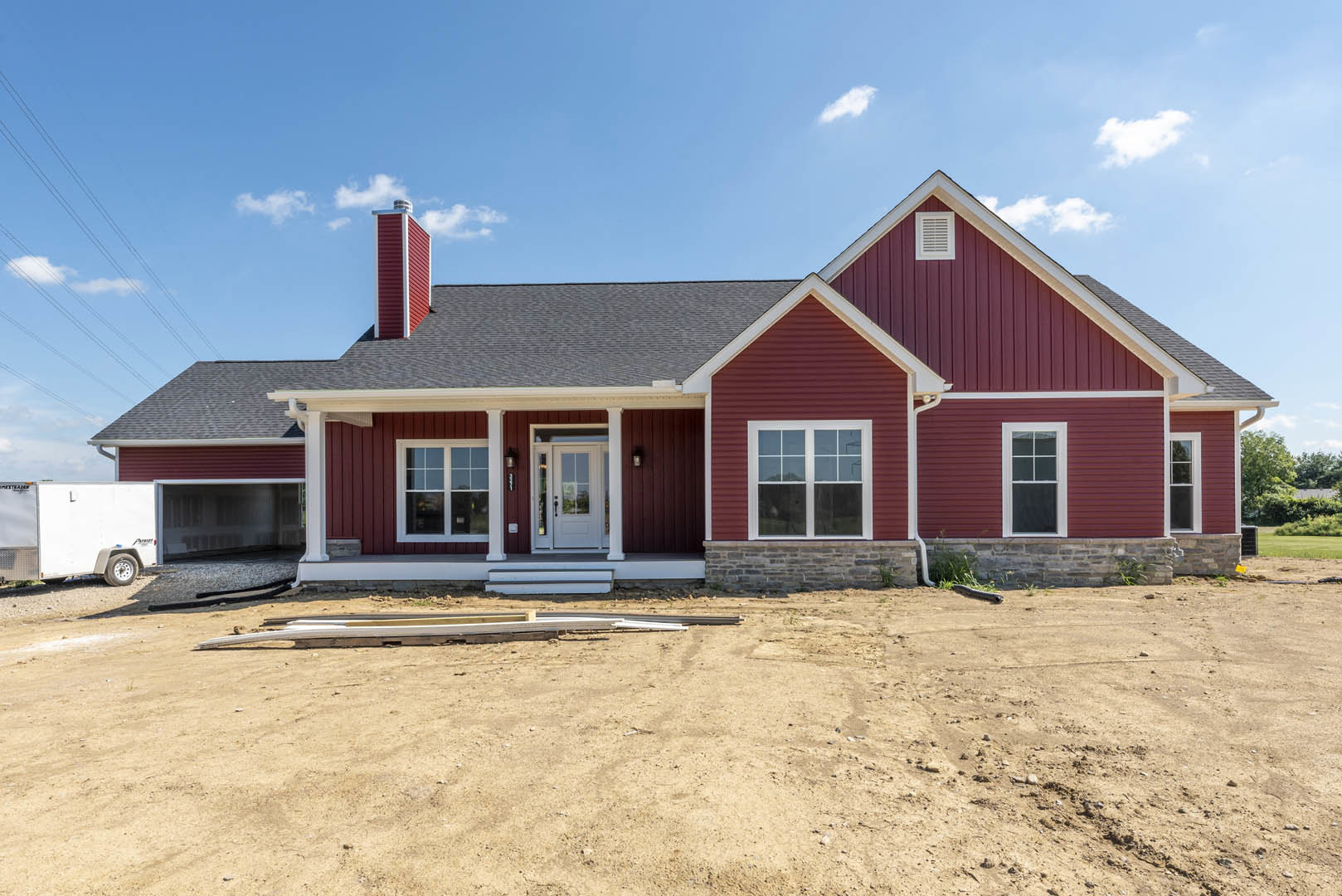 Red house with white trim and glass-paneled white door, close-up window with white frame, dirt area in foreground with pile of wood.