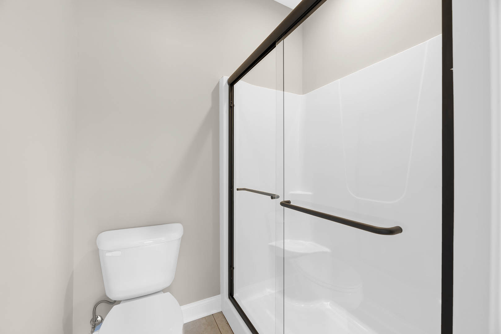 Modern bathroom featuring a frameless glass shower door, white tile walls, toilet with visible tank, black towel bar, and chrome plumbing fixtures