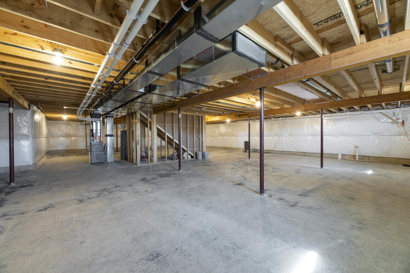 Concrete-floored room with exposed metal ceiling beams, visible ventilation pipes, and scattered buckets; industrial finishes throughout.
