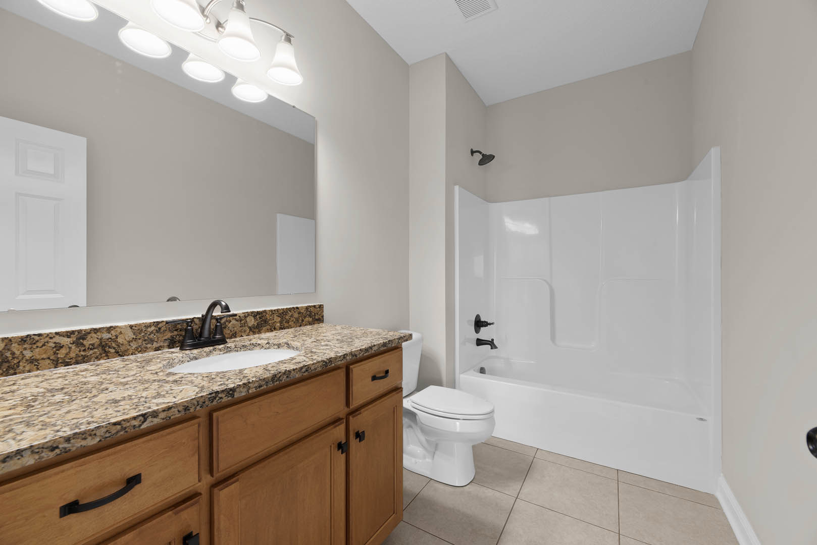 Bathroom with marble countertop, undermount sink, chrome faucet, white tile shower, white toilet, and paneled door