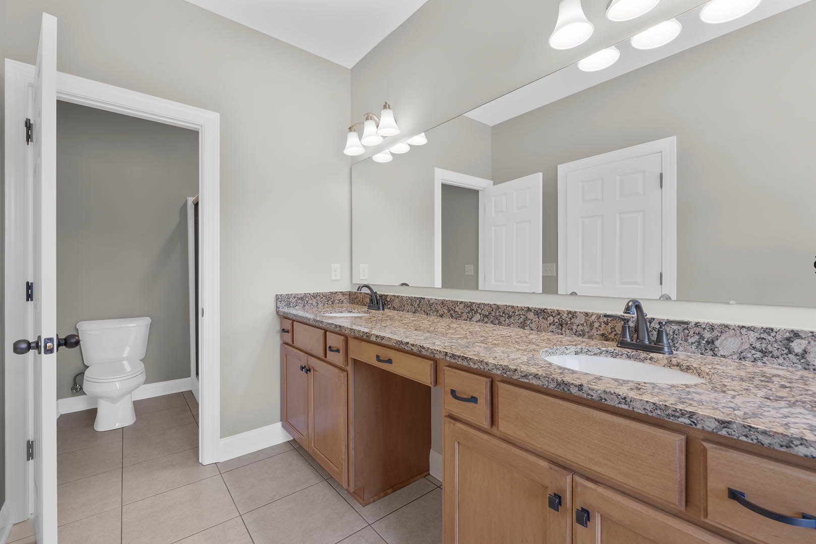 Bathroom with marble countertop, white toilet, white cabinetry, chrome faucet, and wall-mounted row of lights