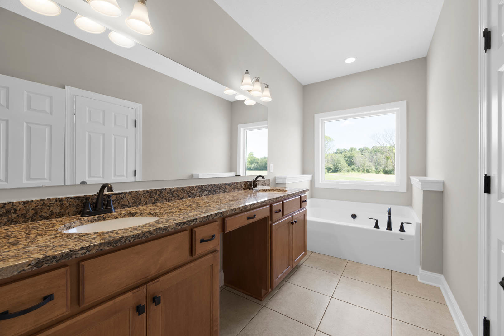 Bathroom with marble countertop, freestanding bathtub with chrome faucets, large window overlooking trees, tile flooring, modern light fixture, and white cabinetry