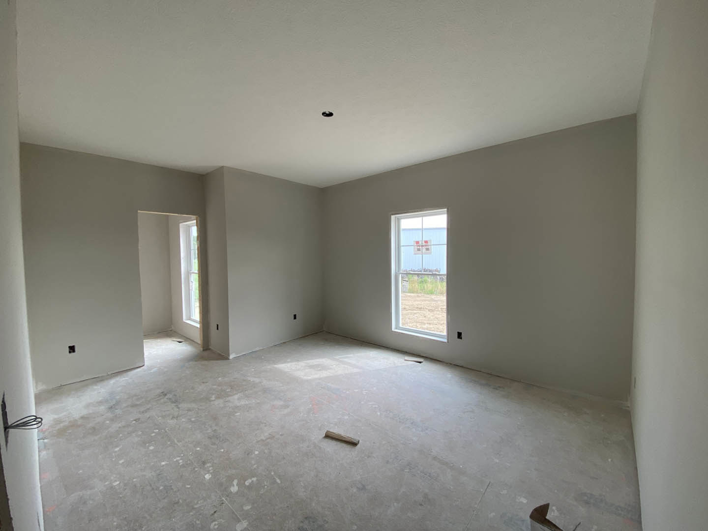 White plaster wall with rectangular window, concrete flooring, wooden stick lying near window, ceiling partially visible