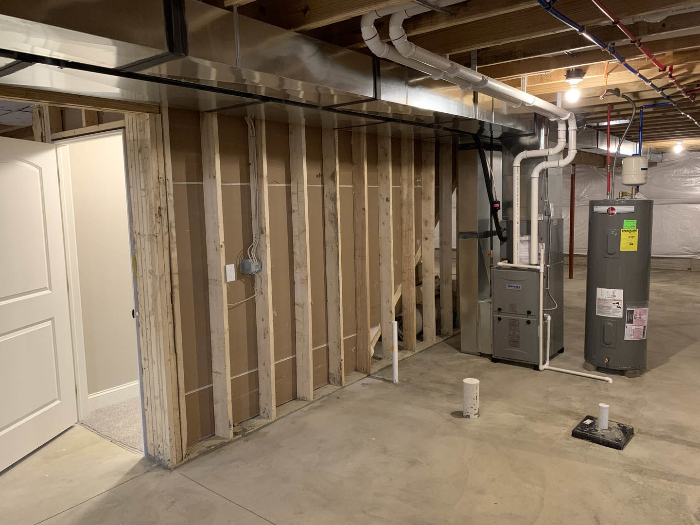 Basement utility room with exposed pipes, large grey cylinder with yellow label, white cylinder with blue tape, white cylinder on black surface, close-up of white door and grey